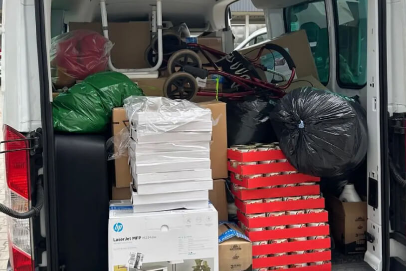 Naložená dodávka: krabice s konzervami, balíky papíru, tiskárna a pytle s pomocí